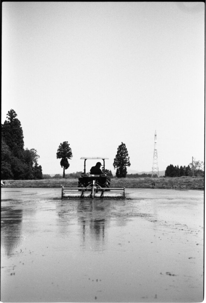 Oratnir・別府倫太郎による祖父を撮ったモノクロフィルム写真作品。田植えの前にトラクターで代掻きをしているところ。撮影場所:新潟県十日町市 使用カメラ：[Nikon New FM2]、フィルム：[ ILFORD HP5 PLUS 400]
